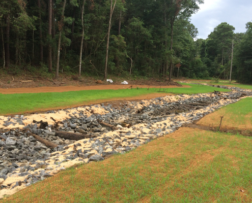 A rock-lined drainage channel bordered by grass.