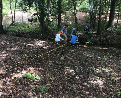 Students measuring a forest stream with a measuring tape and field equipment.